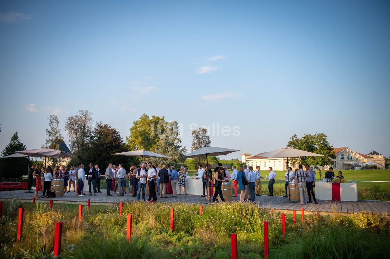 Groupe de personnes rassemblées en extérieur autour de tables sous des parasols, dans un cadre verdoyant et ensoleillé.
