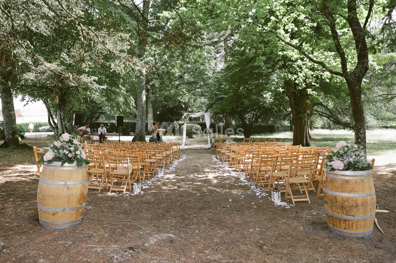 Chaises en bois disposées en rangées dans une clairière, avec une arche décorée pour une cérémonie en plein air.