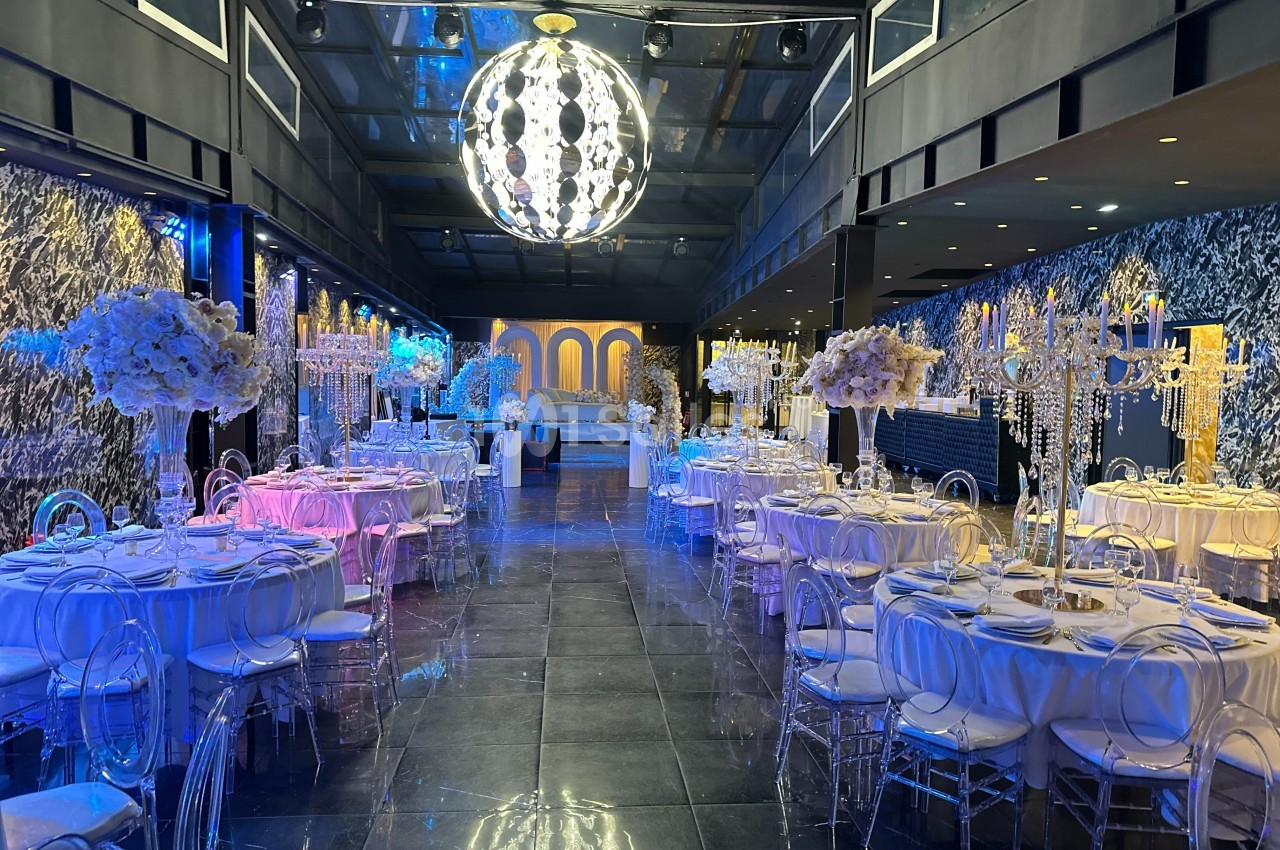 Salle de réception élégante avec tables décorées, chandeliers et éclairage coloré sous un grand lustre central.