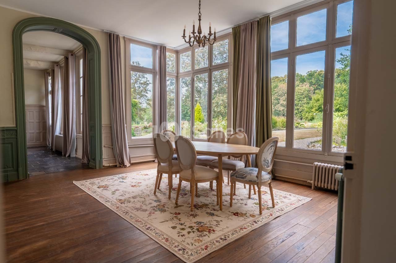 Salle à manger lumineuse avec table ronde, chaises élégantes, grandes fenêtres donnant sur un jardin verdoyant.