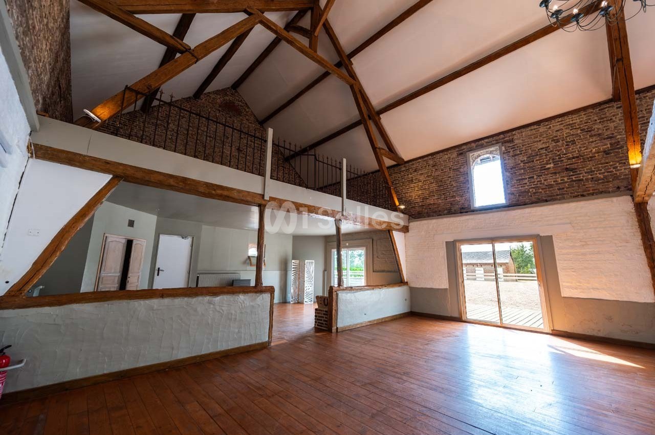 Intérieur d'une grande pièce lumineuse avec poutres apparentes, parquet en bois et mezzanine.