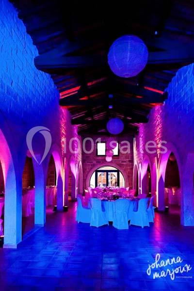 Salle voûtée éclairée par des lumières colorées, avec des tables dressées pour un événement festif.