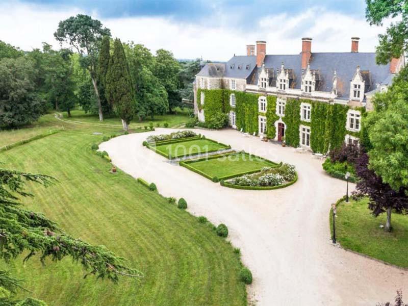 Façade d'un château entouré de jardins paysagers, avec allée gravillonnée et pelouses verdoyantes.