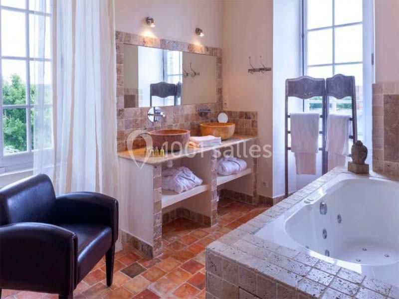 Salle de bain lumineuse avec baignoire à jets, double vasque en pierre, carrelage en terre cuite et grande fenêtre.
