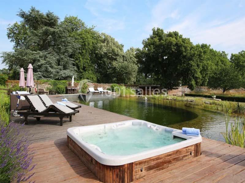 Bain à remous sur une terrasse en bois, entouré de chaises longues, près d'un étang naturel et d'arbres.