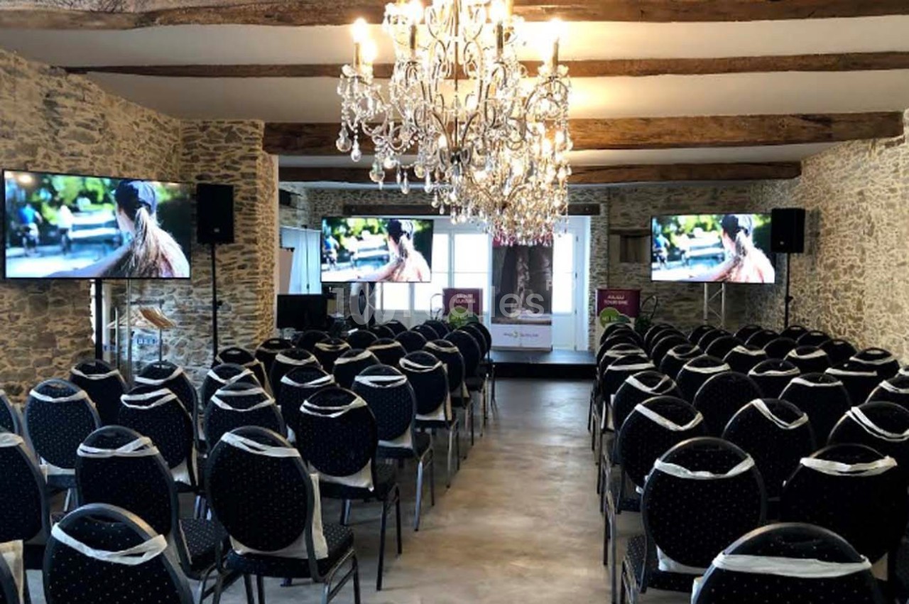 Salle de conférence avec des chaises alignées, écrans plats allumés et un lustre suspendu au plafond.