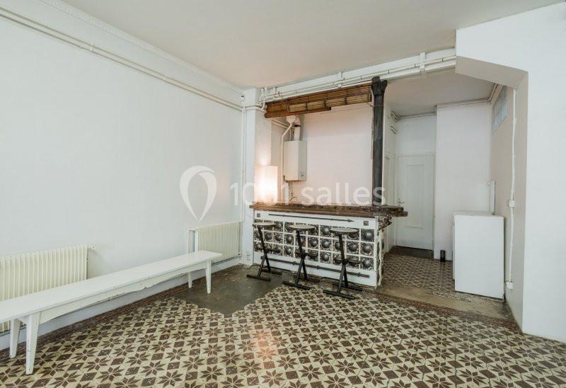 Intérieur d'une pièce avec un sol en carreaux décoratifs, un ancien poêle, un banc et des tabourets devant un comptoir.