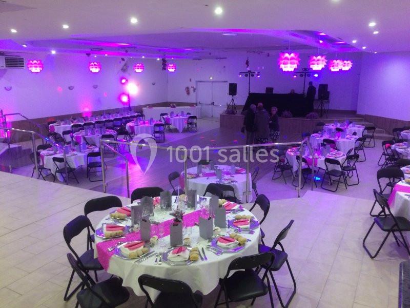 Salle de réception décorée avec des tables rondes dressées, éclairage rose et espace pour une piste de danse.