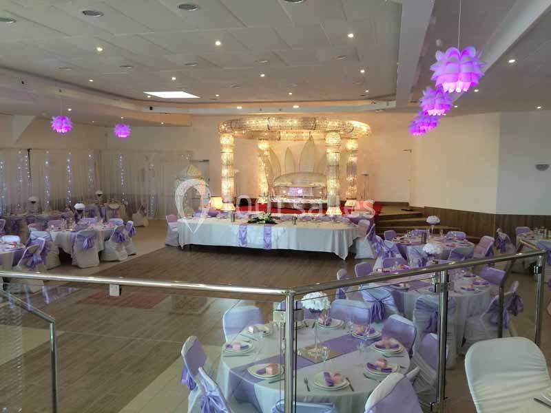 Salle de réception décorée avec des tons violets, tables dressées et scène ornée de lumières et éléments lumineux.