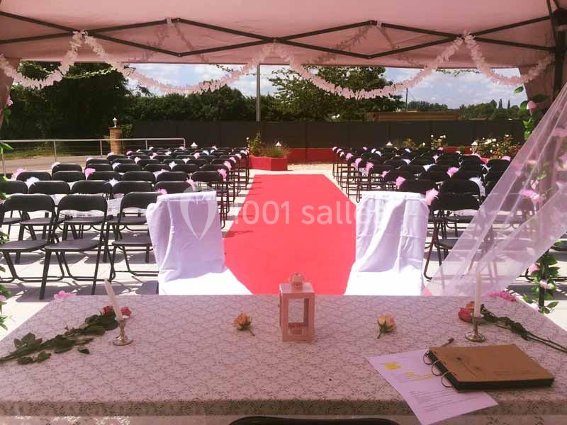 Autel décoré avec nappe blanche, bougies et fleurs, face à une allée rouge bordée de chaises pour une cérémonie en plein air.