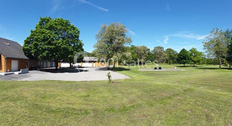 Vue d'un espace vert avec pelouse, arbres, bâtiments en bois et ciel bleu dégagé.
