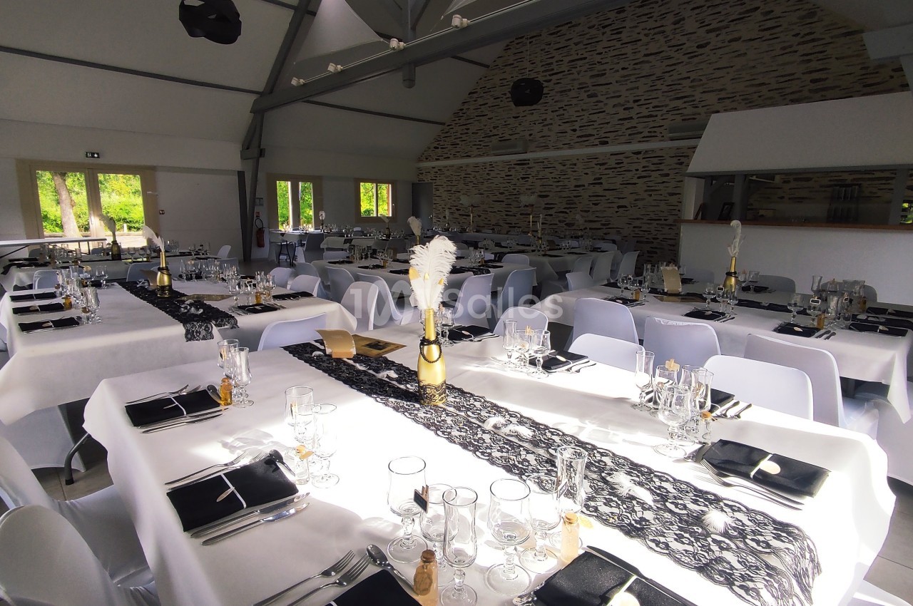 Salle de réception décorée avec des tables dressées, nappes blanches et chemins de table noirs en dentelle.