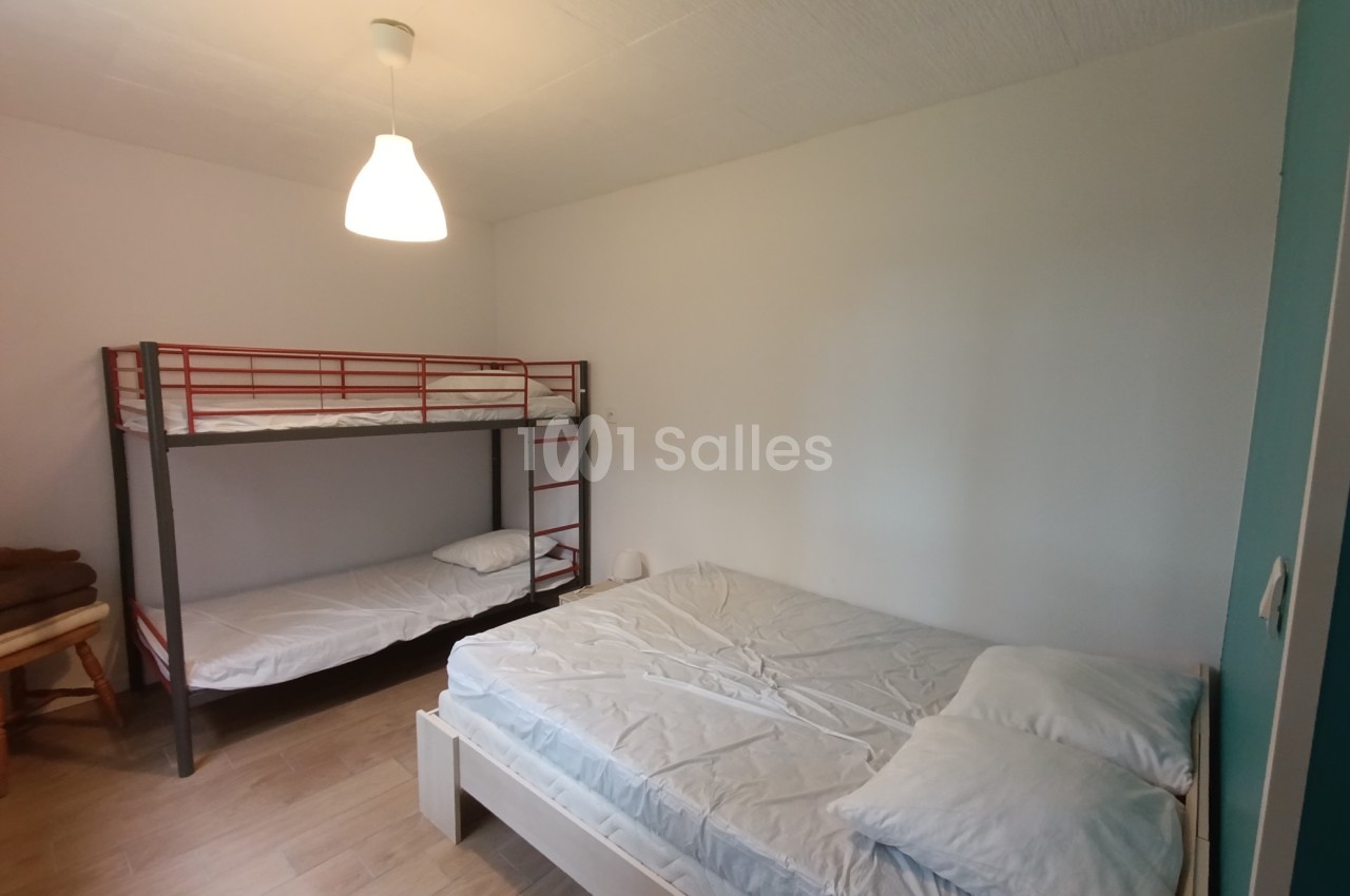Chambre avec un lit double, un lit superposé, murs blancs, sol en bois clair et lampe suspendue.
