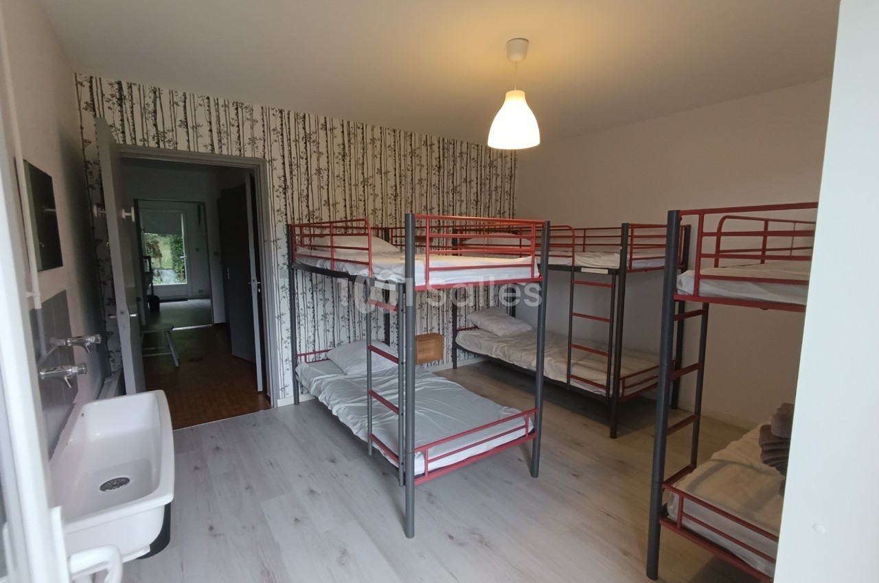 Dortoir avec lits superposés en métal, lavabo, parquet clair et papier peint à motif de bouleaux.