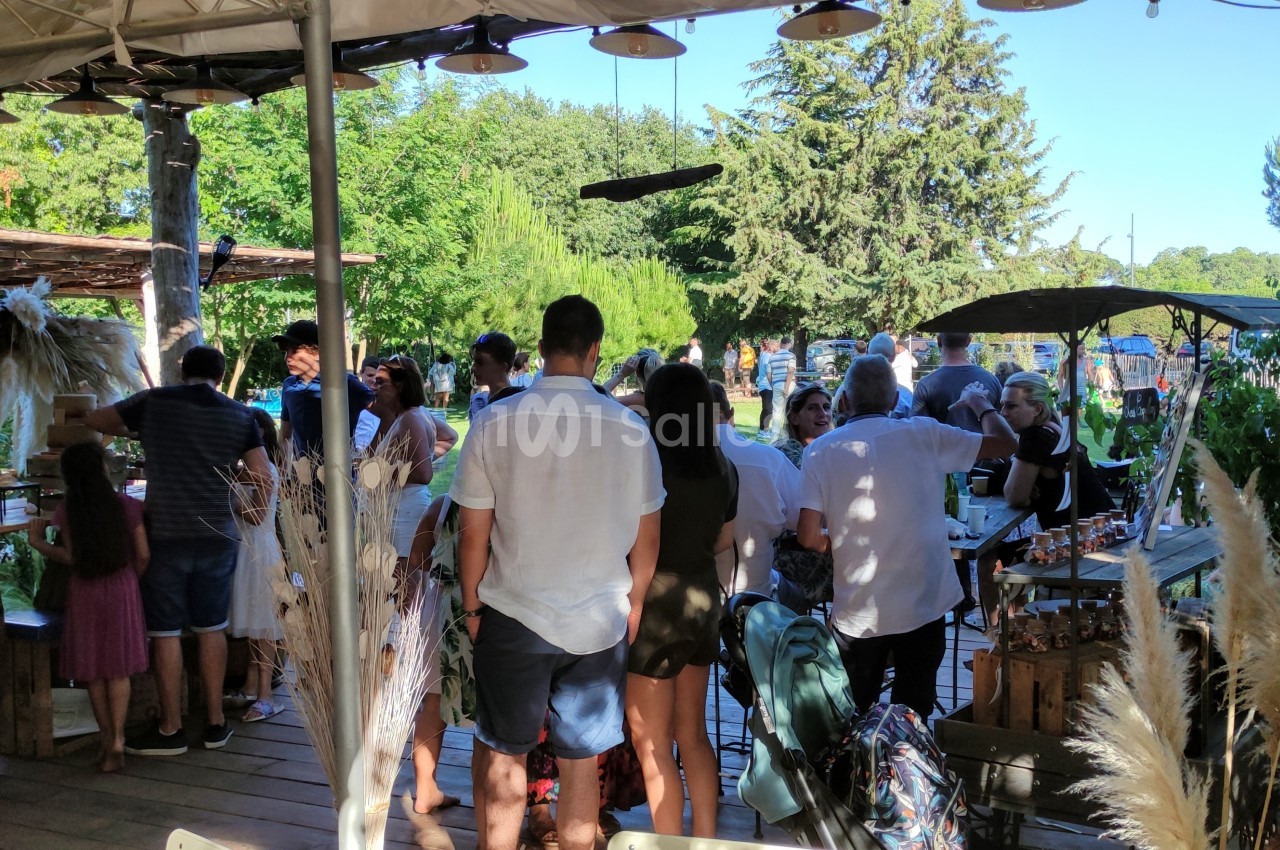 Groupe de personnes rassemblées dans un marché en plein air, entourées de végétation et de stands artisanaux.