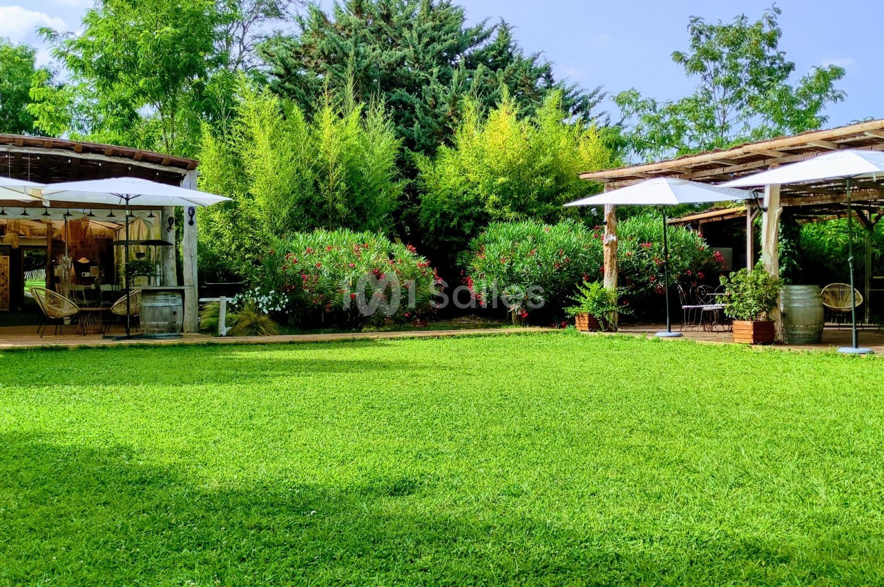 Deux pergolas en bois avec parasols blancs entourées de végétation luxuriante et une pelouse verte au premier plan.