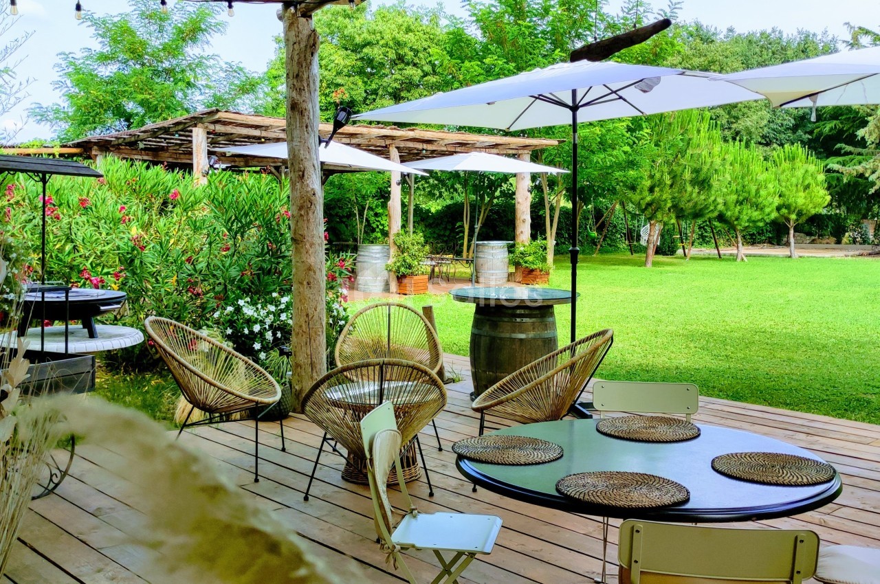 Terrasse en bois avec tables et chaises entourées de verdure, ombragée par des parasols blancs et des pergolas.