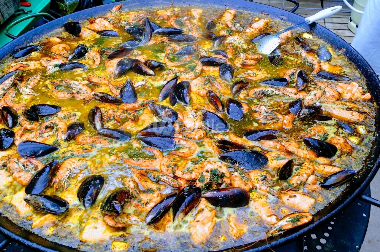 Grande poêle de paella garnie de moules, crevettes et morceaux de poulet, cuite avec des épices et du bouillon.