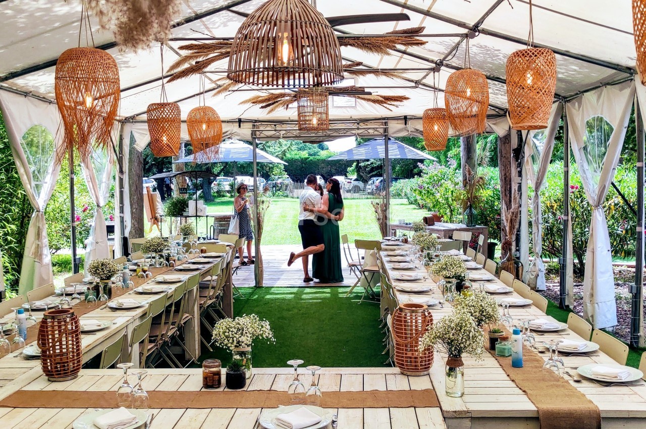 Salle de réception en plein air sous une tente, décorée avec des lampes en osier et des tables dressées pour un événement.