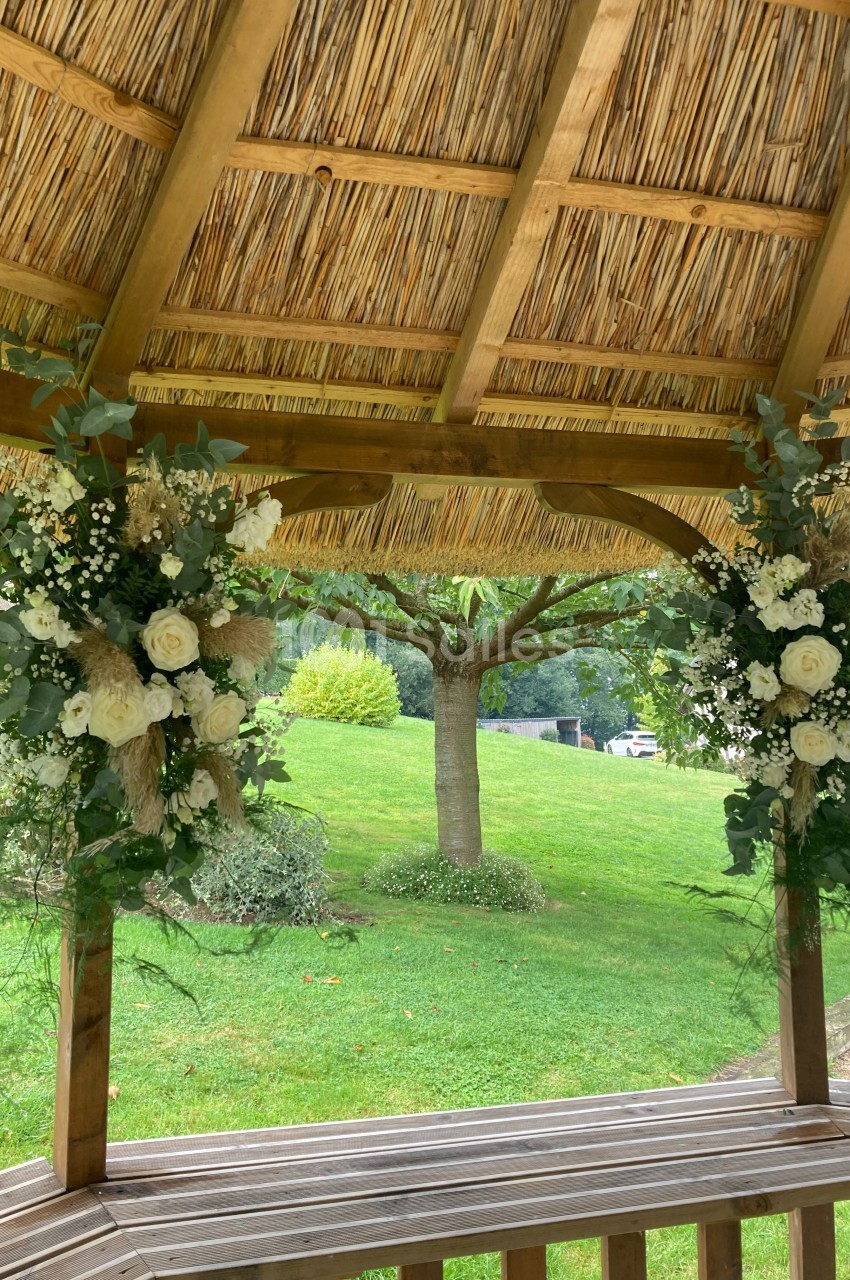 Deux arrangements floraux blancs et verts décorent une pergola en bois avec vue sur un jardin verdoyant.