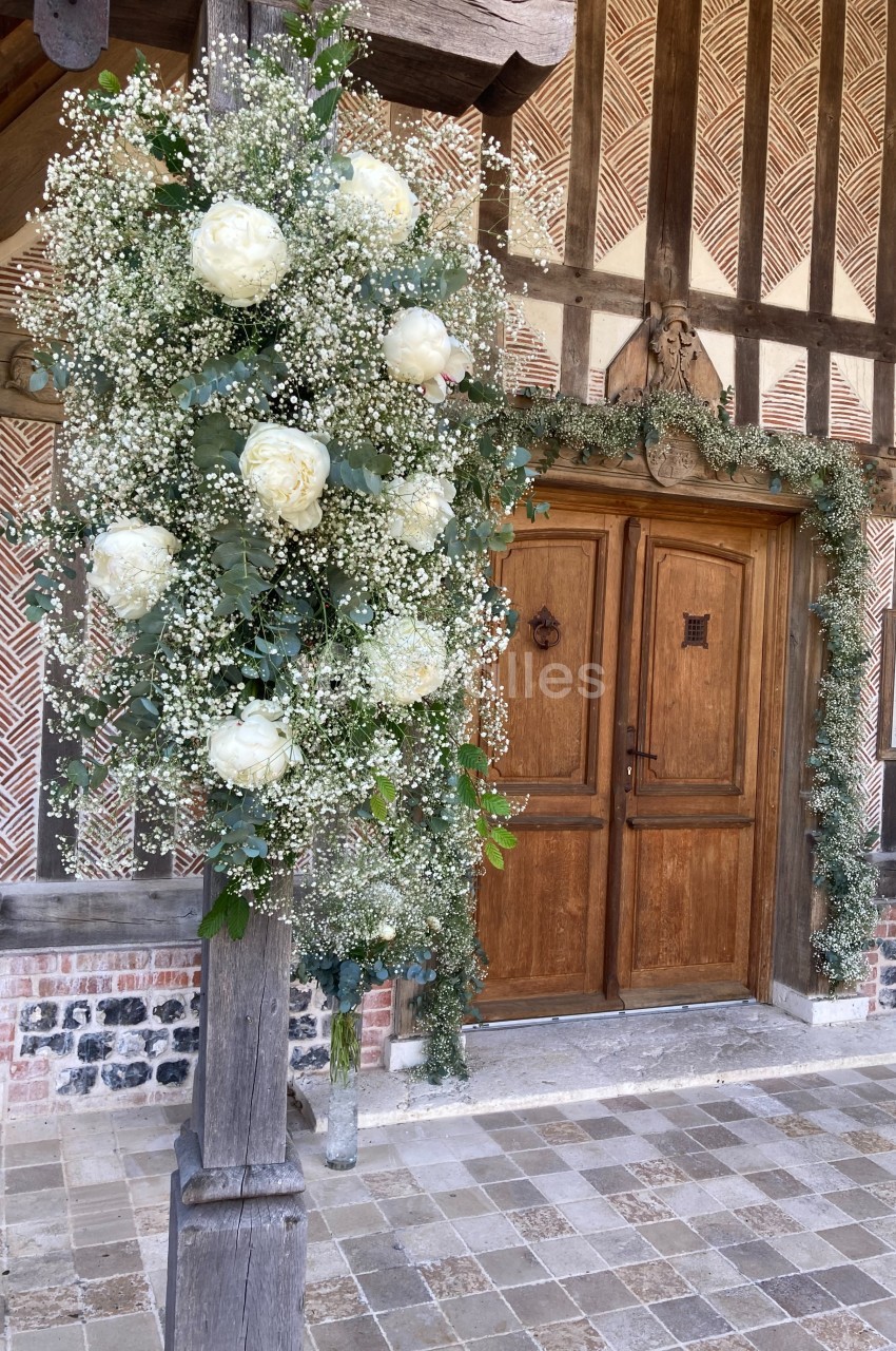 Décoration florale avec pivoines blanches et gypsophile suspendue près d'une porte en bois dans un cadre rustique.