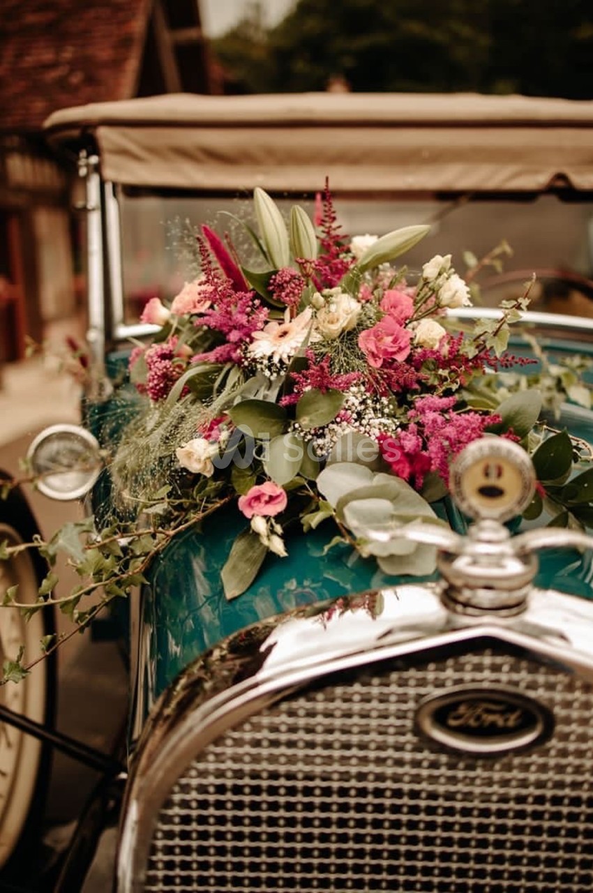 Arrangement floral coloré sur le capot d'une voiture ancienne verte avec une calandre en métal.