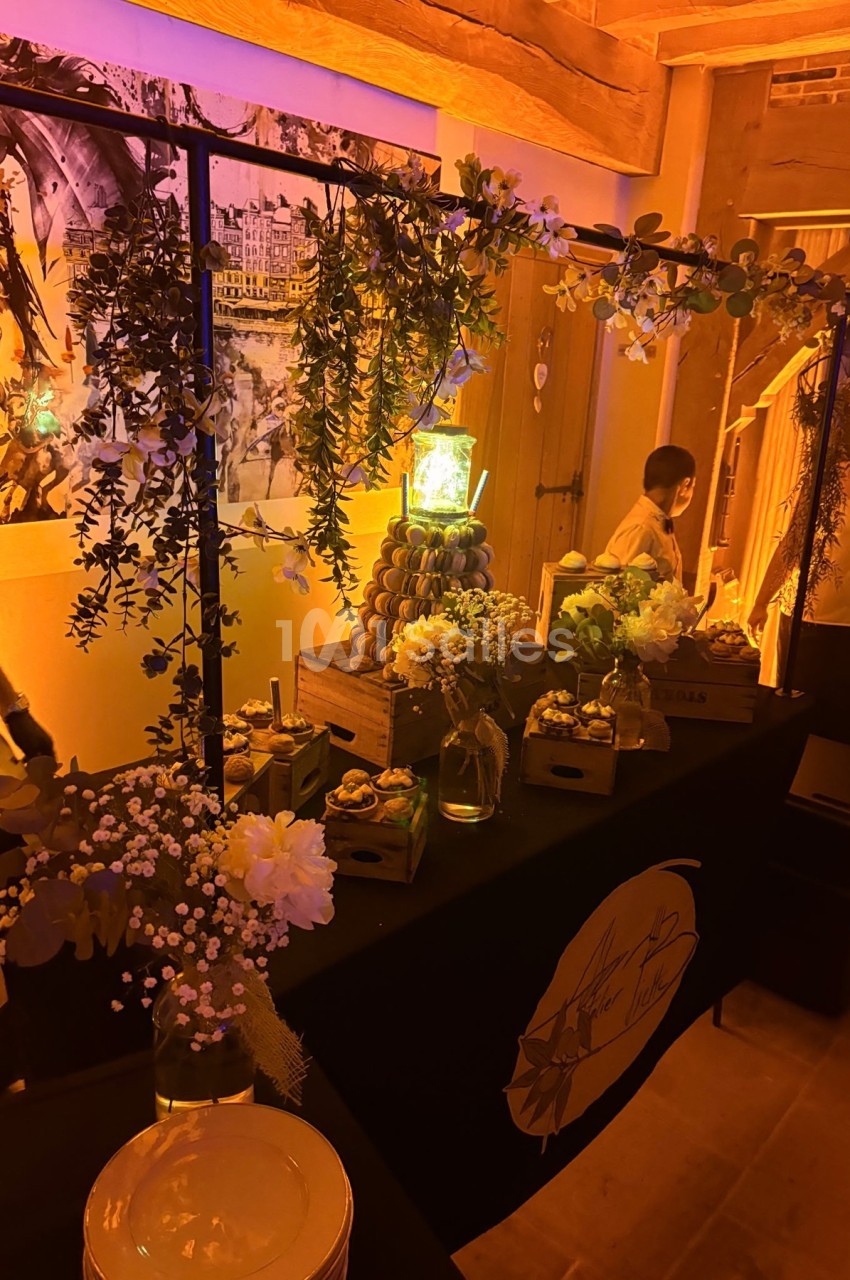 Table décorée avec des fleurs, des plantes suspendues et des desserts, dans une ambiance chaleureuse et tamisée.