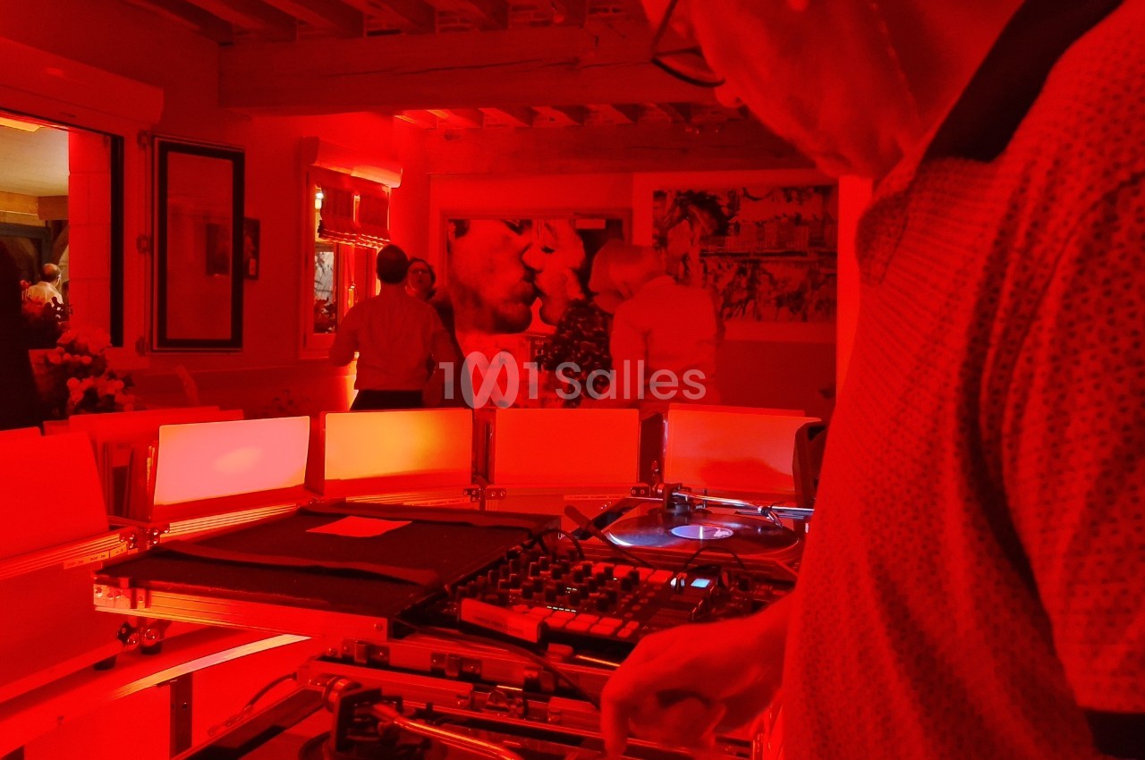 Un DJ mixe des vinyles dans une pièce éclairée de lumière rouge, avec des personnes en arrière-plan.