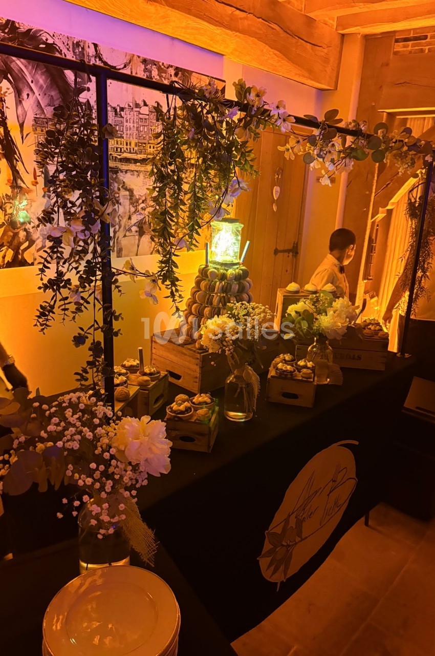 Table décorée avec des fleurs, des plantes suspendues et des desserts, dans une ambiance chaleureuse et éclairage tamisé.