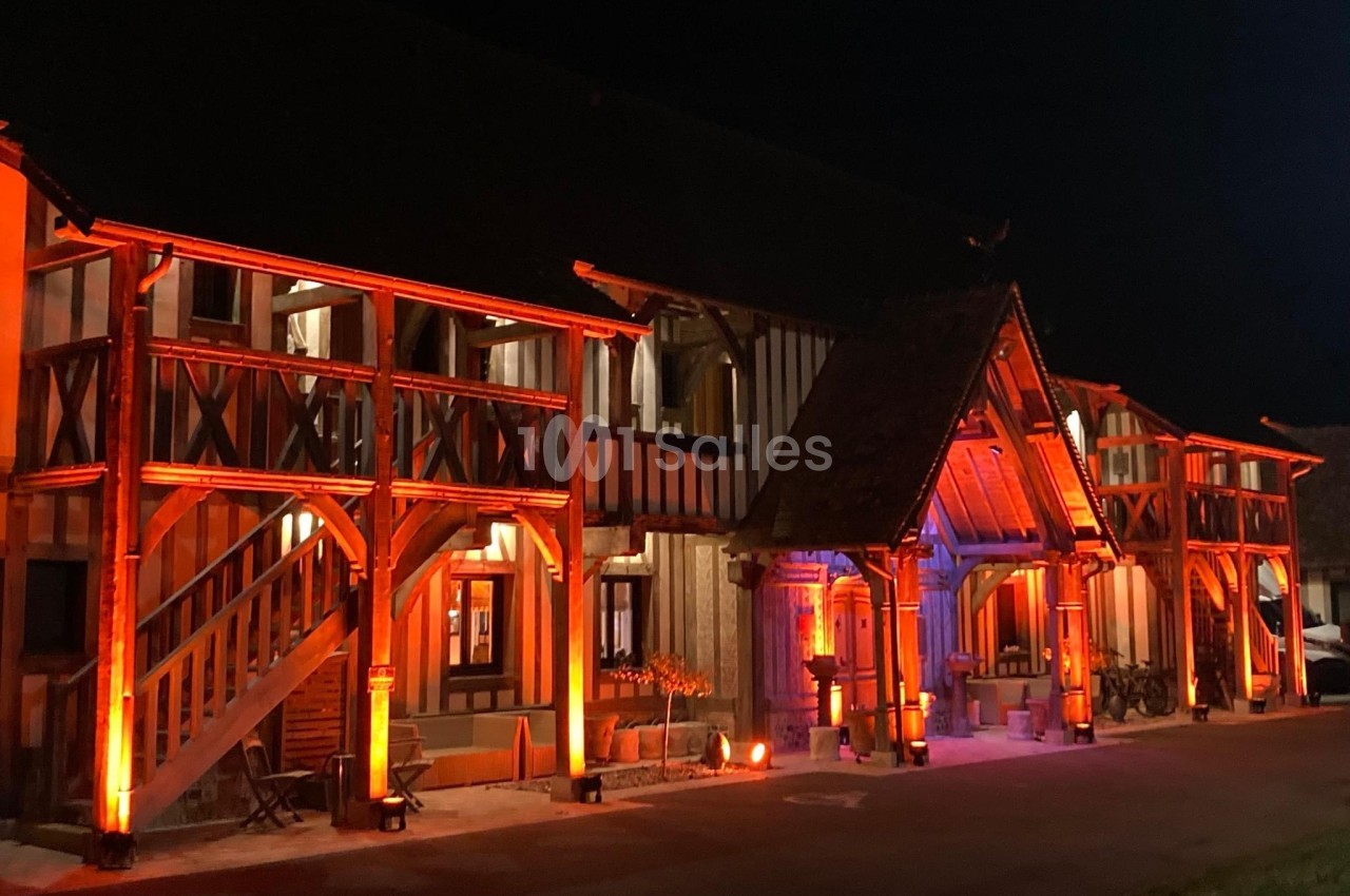 Façade d'un bâtiment à colombages éclairée par des lumières orange et rouges dans un environnement nocturne.