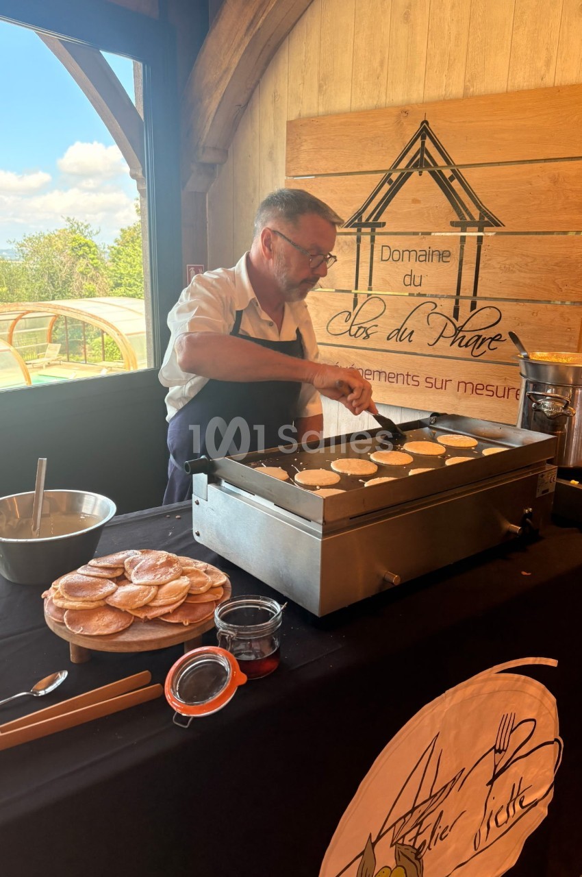 Un cuisinier prépare des crêpes sur une plaque chauffante lors d'un événement dans un cadre en bois lumineux.