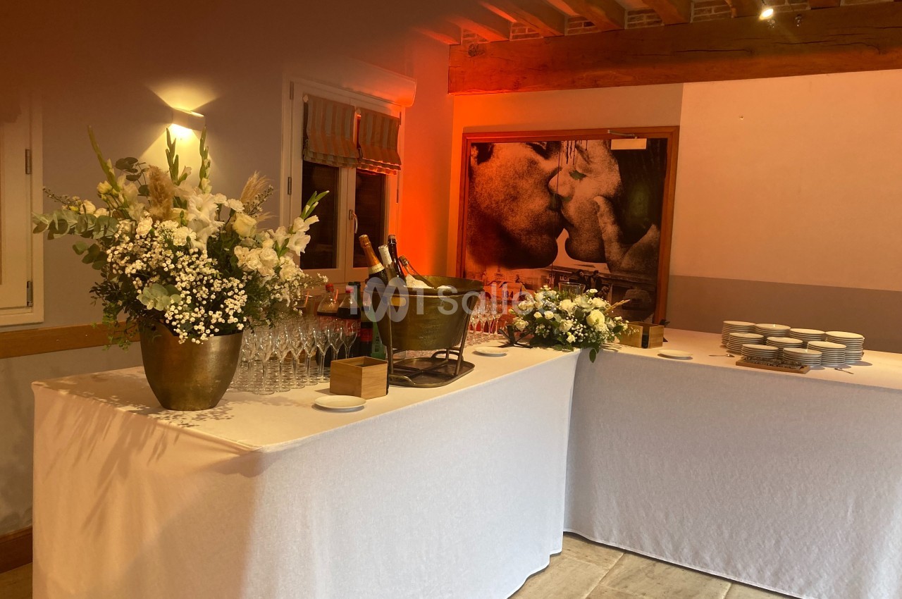 Table dressée avec nappes blanches, fleurs, seau à champagne, verres et assiettes dans une salle éclairée chaleureusement.