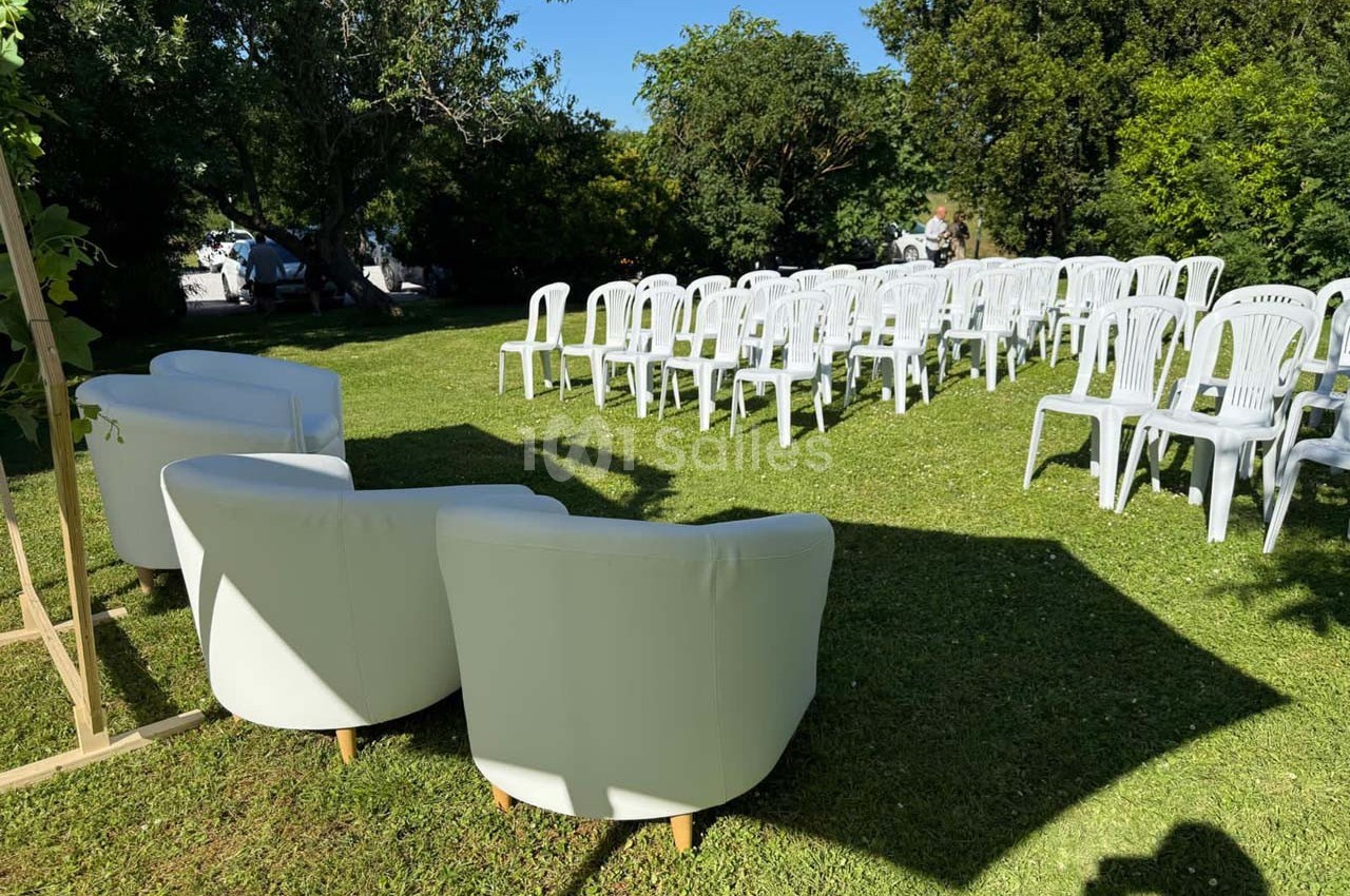 Chaises blanches disposées en rangées sur une pelouse, avec des fauteuils blancs au premier plan, sous un ciel ensoleillé.