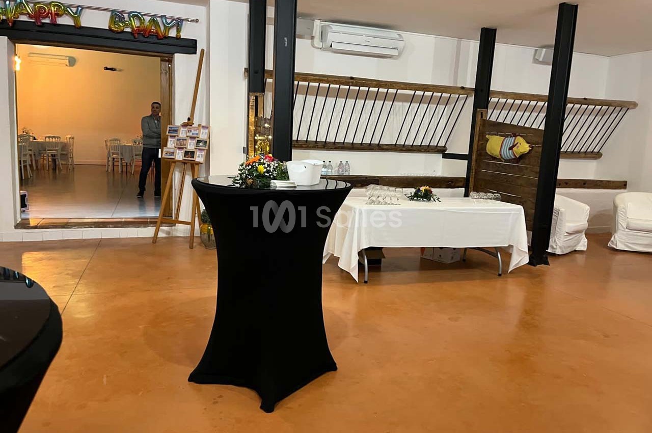 Salle de réception avec table haute noire au premier plan, buffet dressé et décorations murales en arrière-plan.
