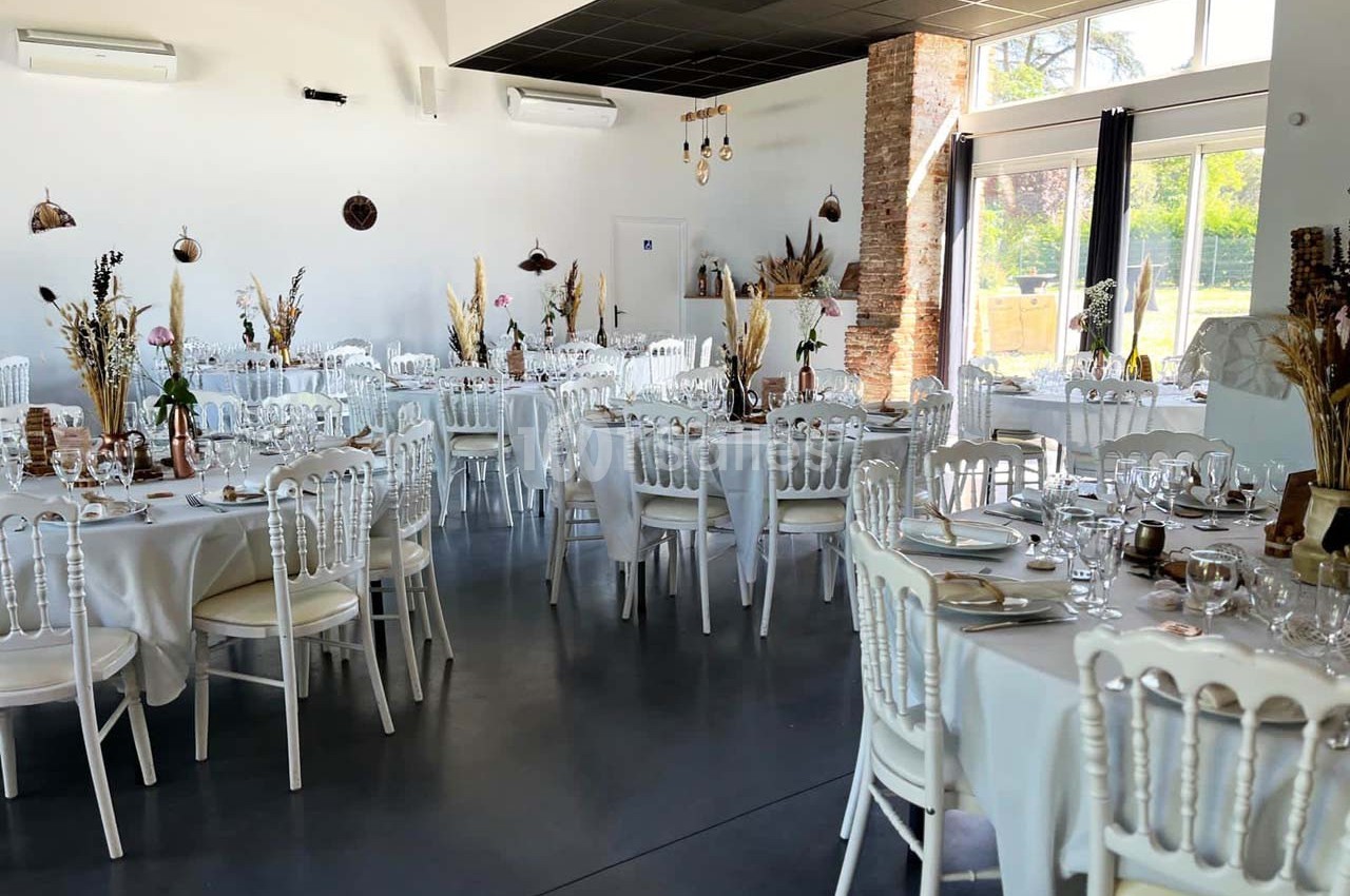 Salle de réception décorée avec des tables rondes dressées, nappes blanches et éléments naturels.