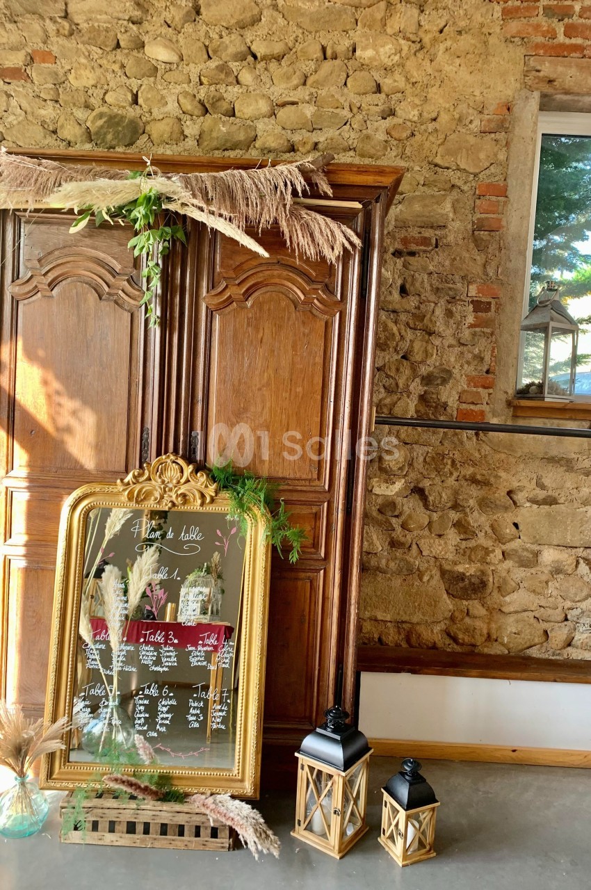 Armoire en bois rustique avec un plan de table encadré doré, décoré de plantes et pampas, dans une pièce en pierre.