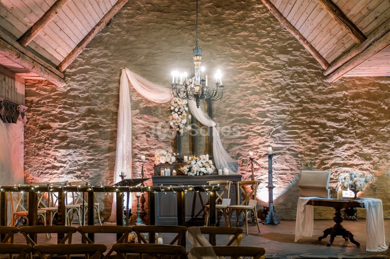 Salle en pierre avec un autel décoré de fleurs et de voilages, éclairée par un lustre et des lumières tamisées.