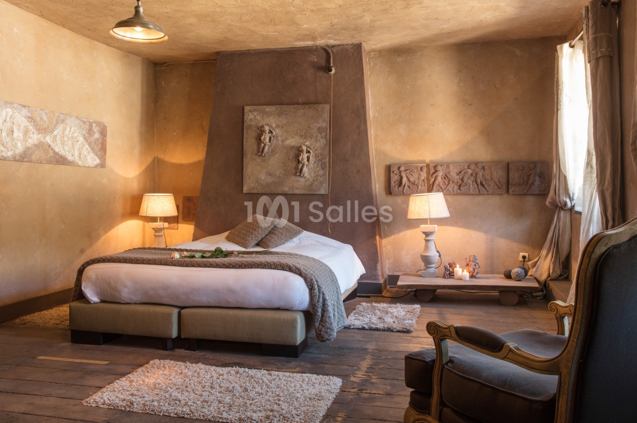 Chambre chaleureuse avec lit double, murs en terre cuite, éclairage doux et décorations murales artistiques.