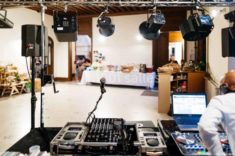 Matériel de DJ avec platines et ordinateur installé dans une salle, éclairée par des projecteurs suspendus.
