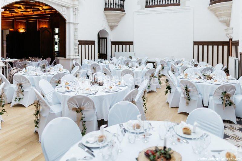 Salle de réception élégante avec tables rondes dressées, nappes blanches et décorations florales.