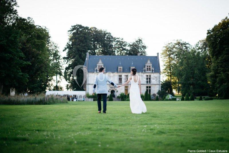 Un couple marche main dans la main sur une pelouse, avec un château en arrière-plan entouré d'arbres.