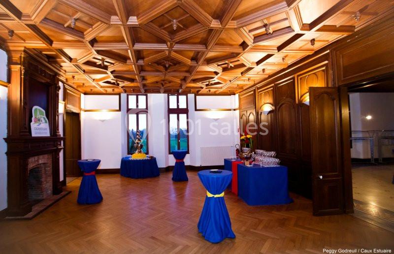 Salle avec parquet, plafond à caissons en bois, tables hautes décorées et buffet installé près d'une cheminée.