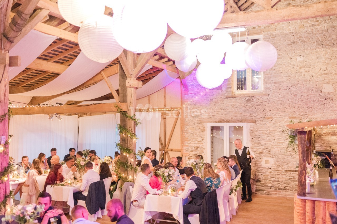 Salle de réception décorée avec des guirlandes lumineuses et des lanternes, des invités assis à des tables festives.