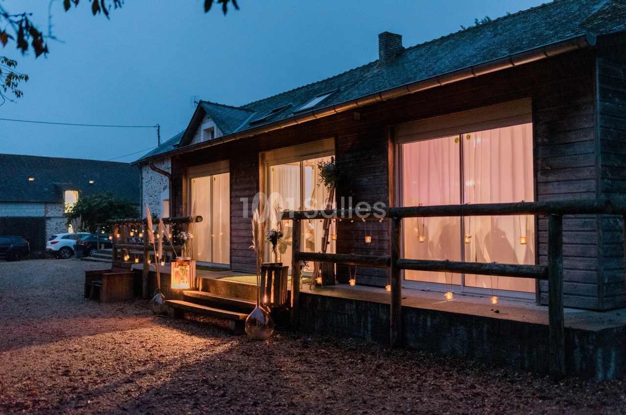 Façade d'une maison en bois éclairée par des lumières tamisées et des bougies au crépuscule.