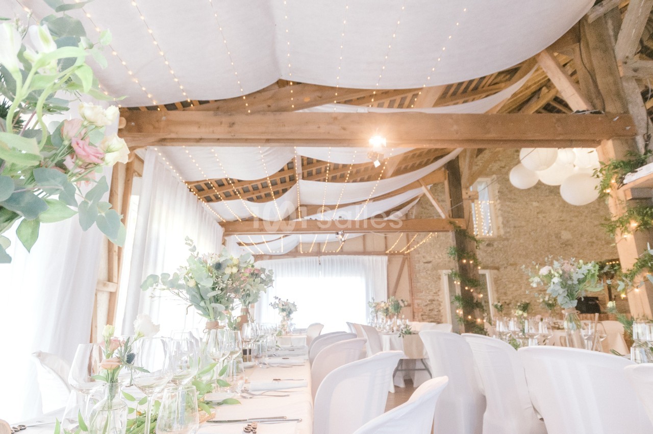 Salle de réception lumineuse décorée avec des guirlandes lumineuses, des fleurs et des tables dressées pour un événement.