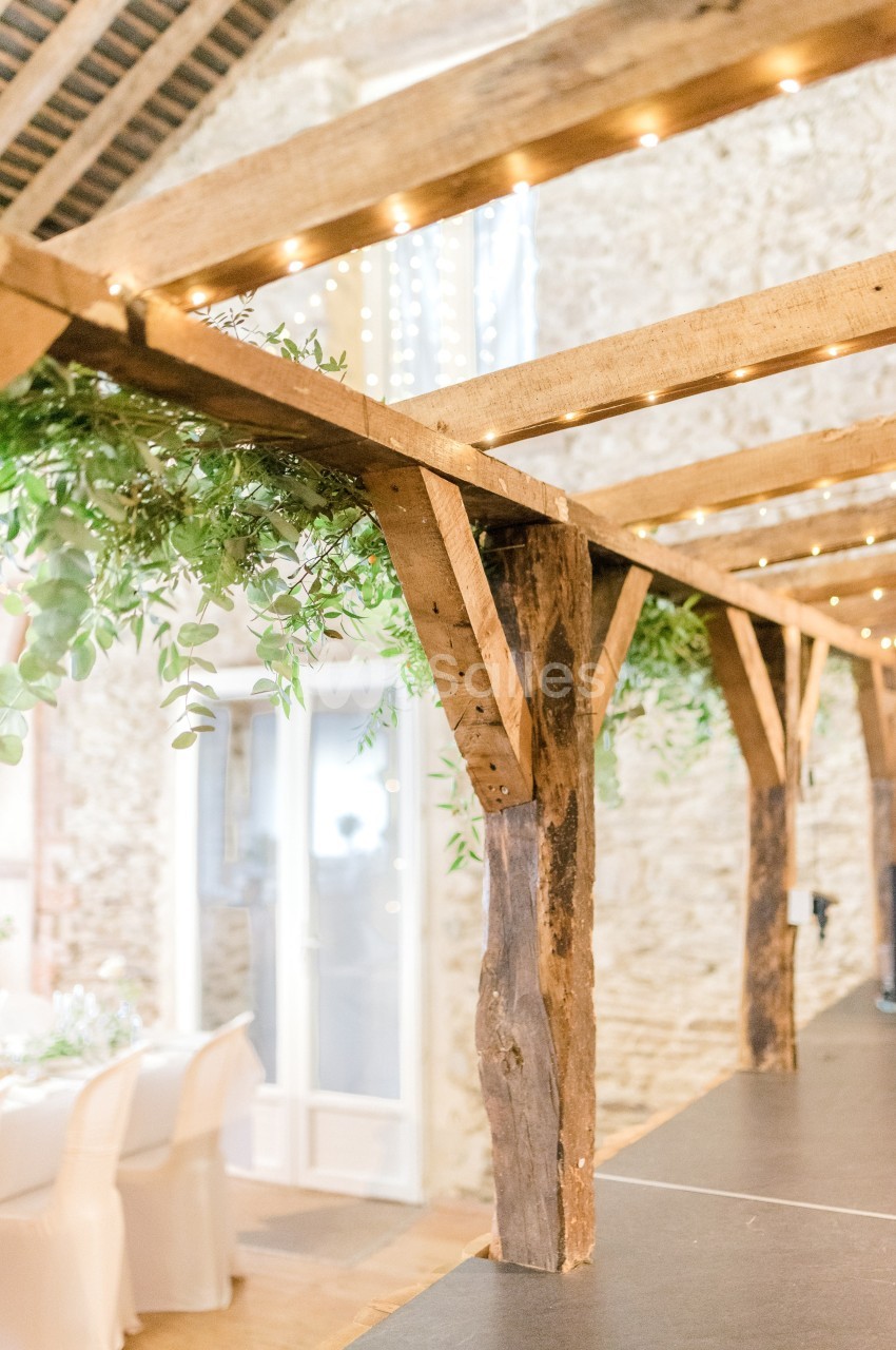 Structure en bois décorée de guirlandes lumineuses et de feuillage, dans une salle aux murs en pierre.