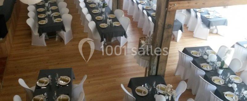 Salle de réception avec tables dressées, nappes noires, chaises blanches et parquet en bois clair.