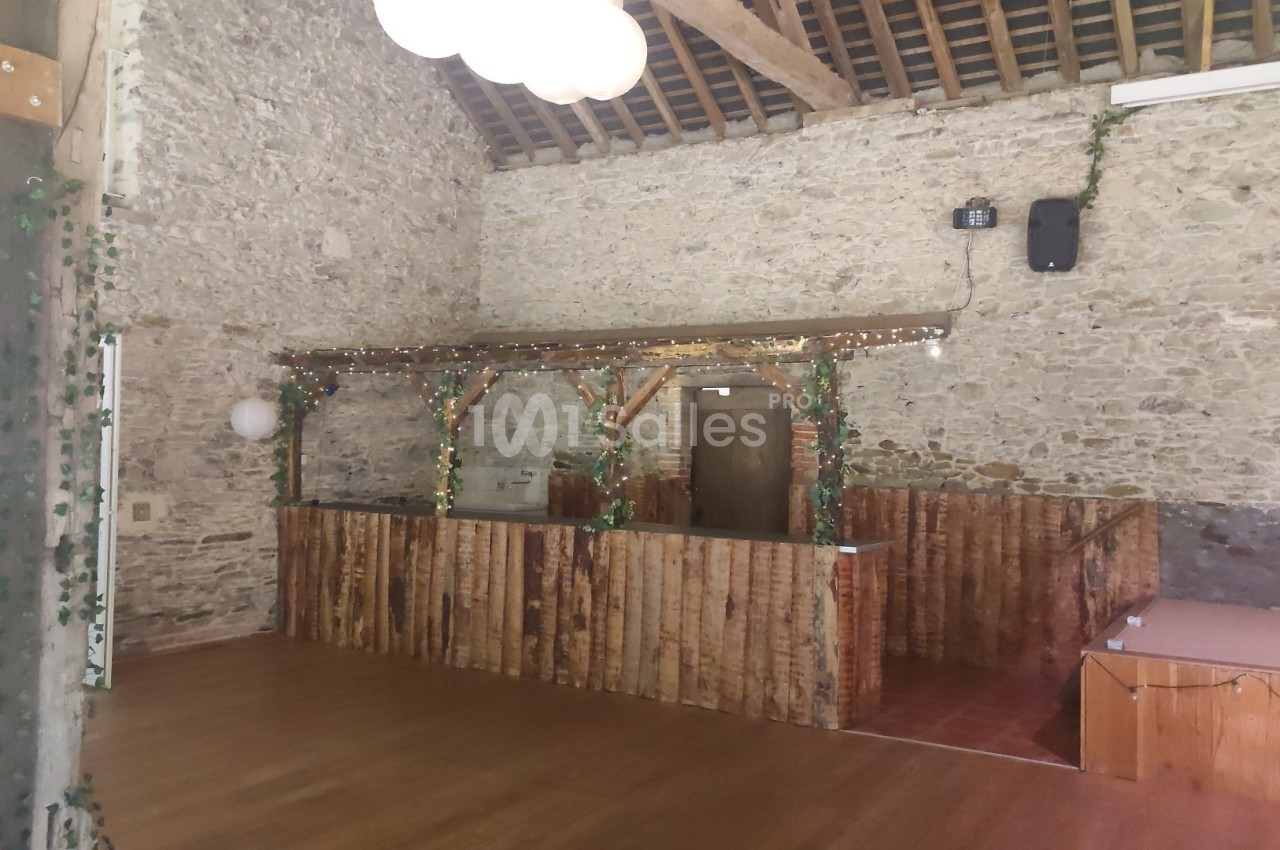 Espace intérieur avec murs en pierre, parquet en bois et comptoir décoré de guirlandes lumineuses et de feuillage.