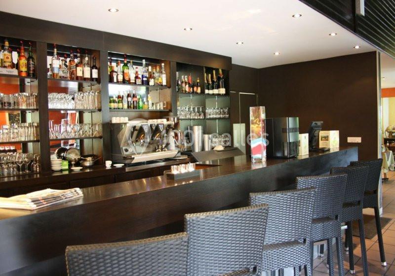 Bar moderne avec comptoir en bois sombre, tabourets tressés, étagères remplies de bouteilles et machine à café.