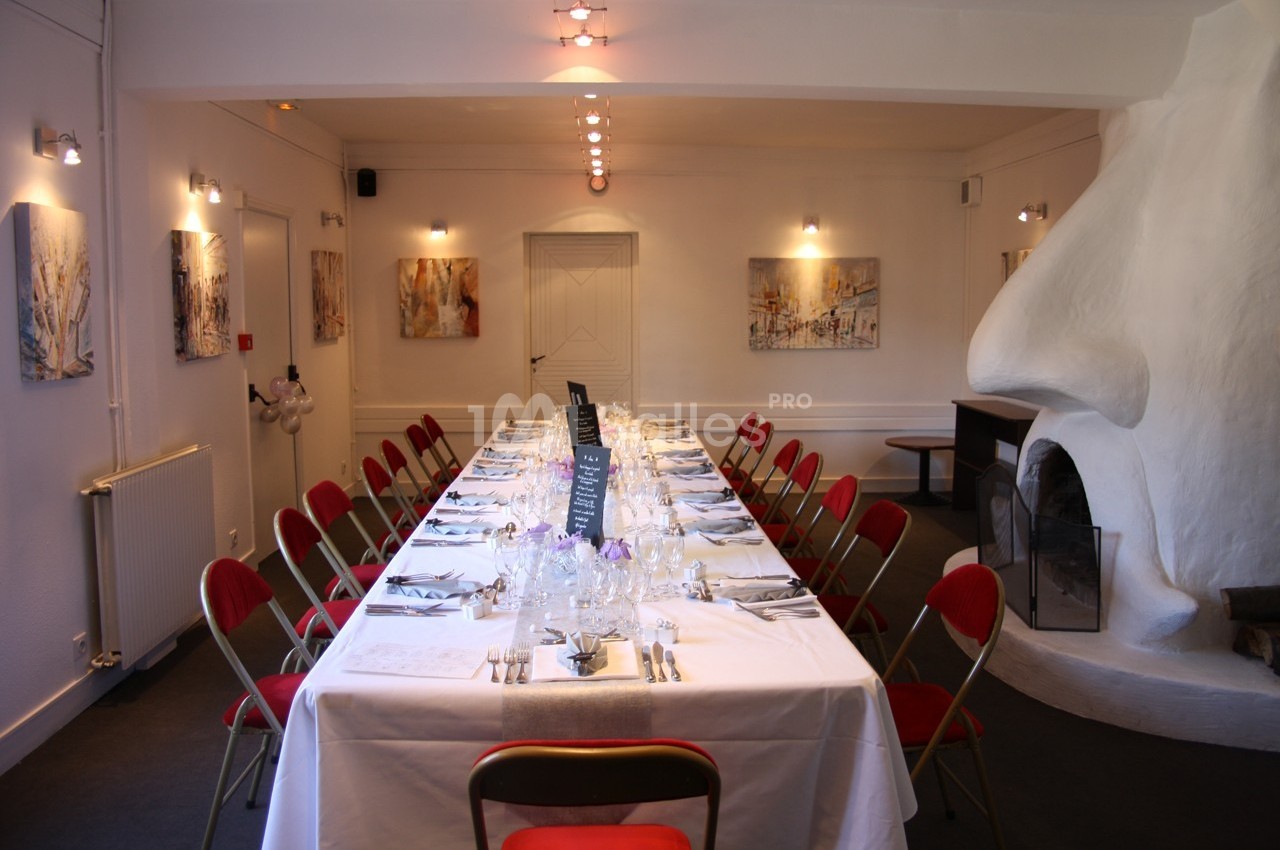 Salle de réception avec une grande table dressée, entourée de chaises rouges, et décorée de peintures murales.